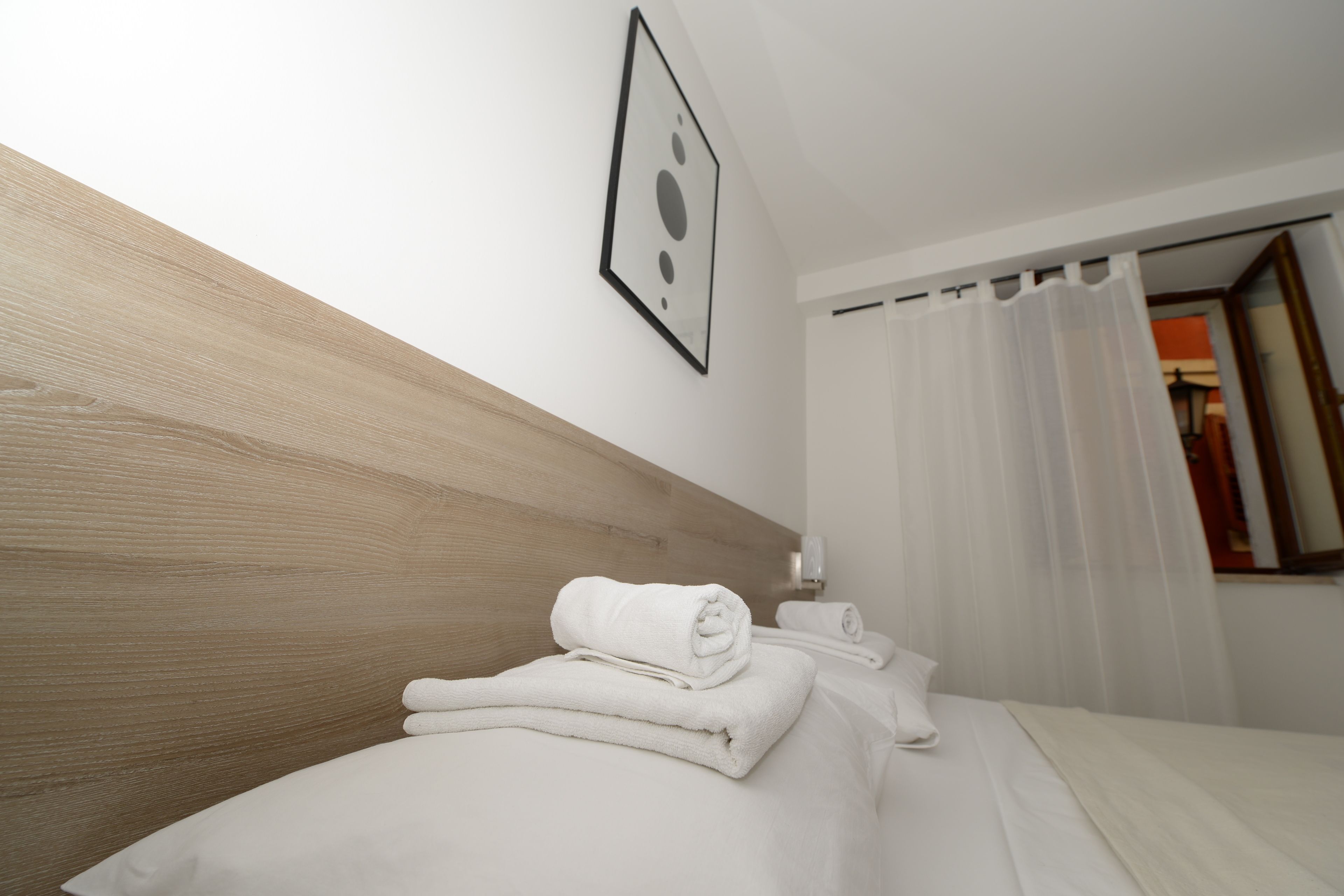A neatly made bed with white linens and towels, a wooden headboard, and a framed picture on the wall.