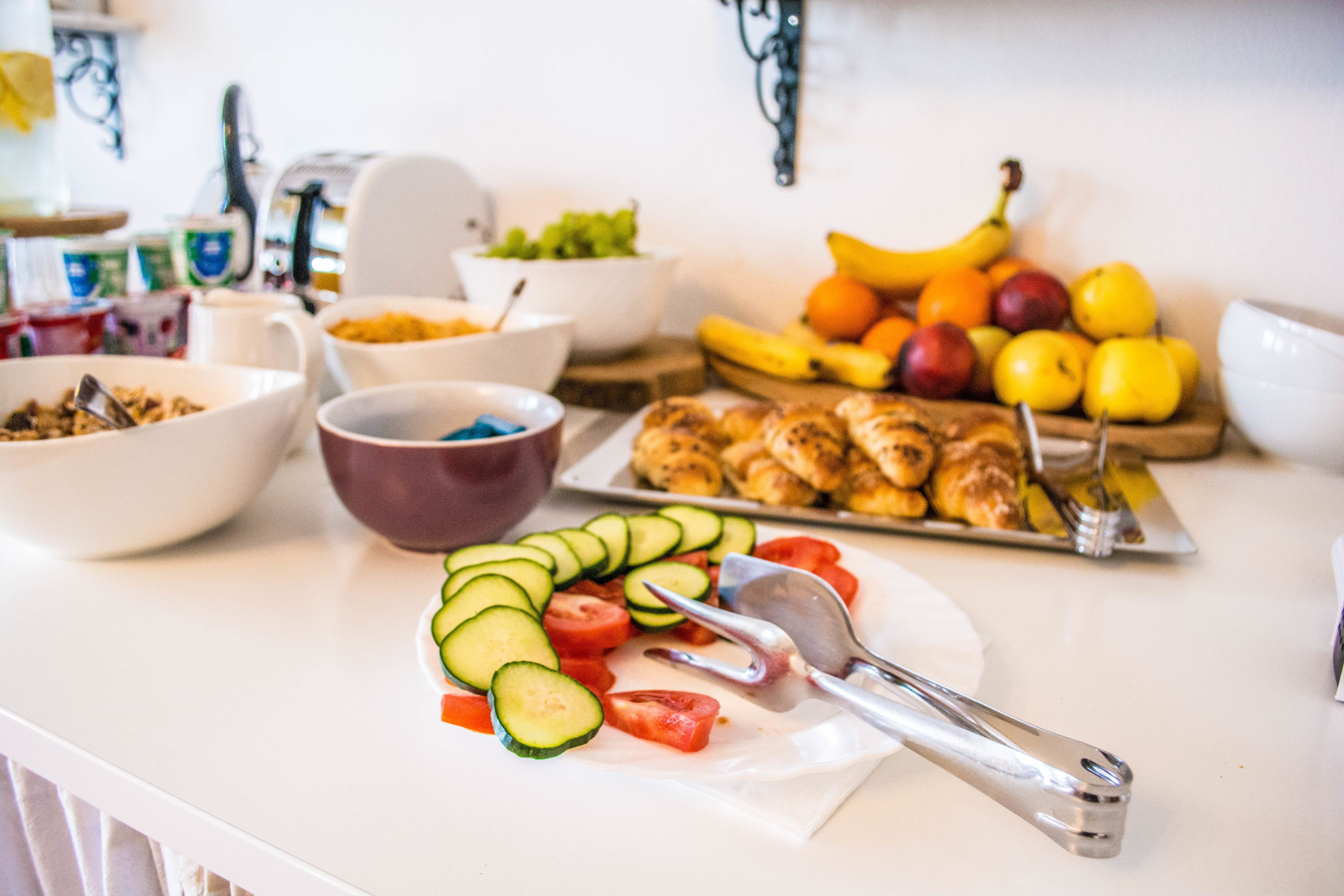 Una encimera de cocina con diversos alimentos, entre ellos verduras cortadas, frutas y un plato de croissants.