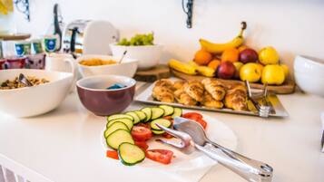 Una encimera de cocina con diversos alimentos, entre ellos verduras cortadas, frutas y un plato de croissants.