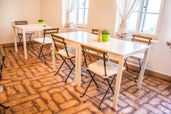 Un comedor con piso de ladrillo, mesas y sillas blancas.