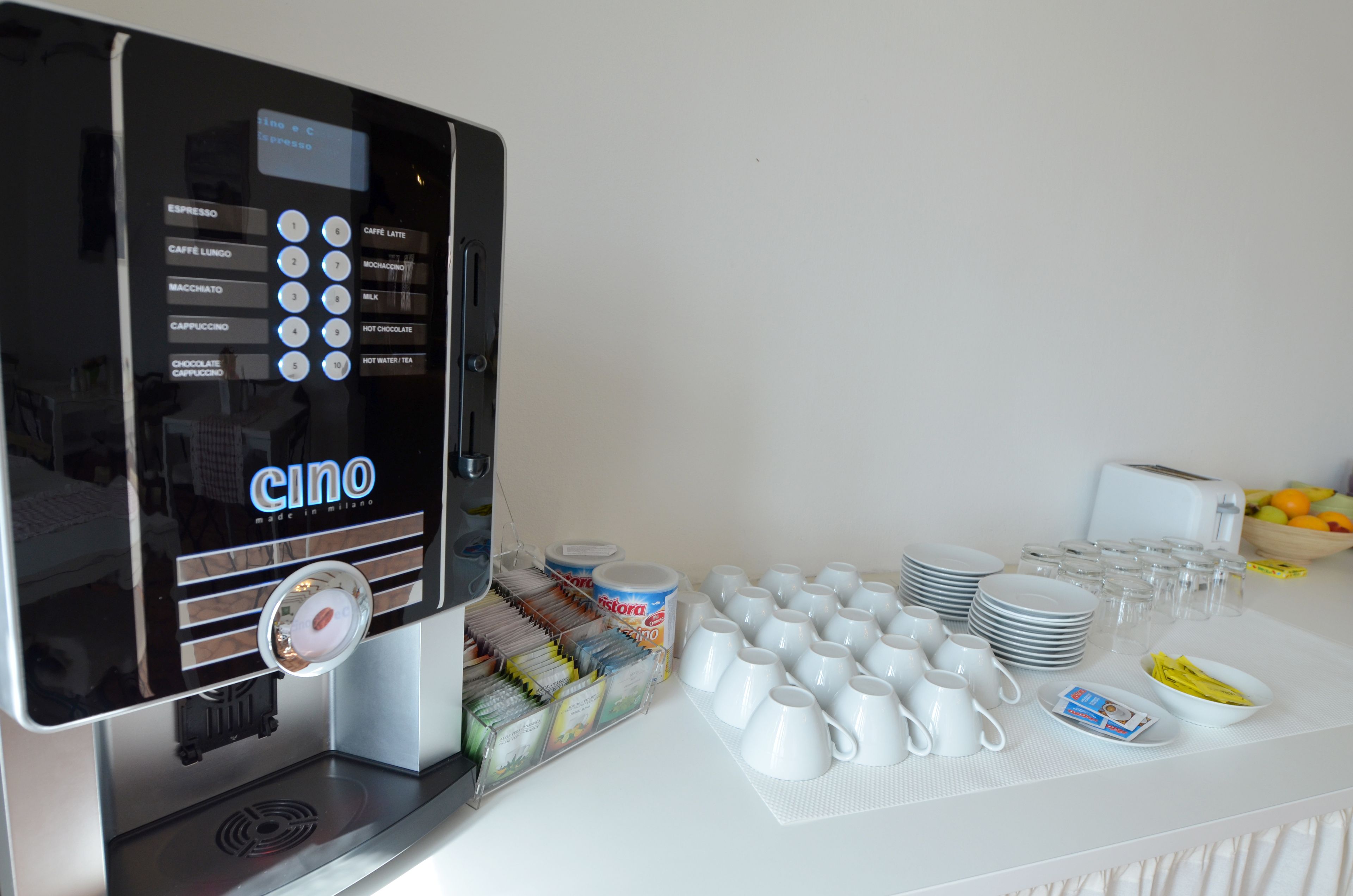 Een koffieapparaat met diverse dranken, een assortiment melkpakken en een tafel gedekt met borden, kopjes en toevoegingen.