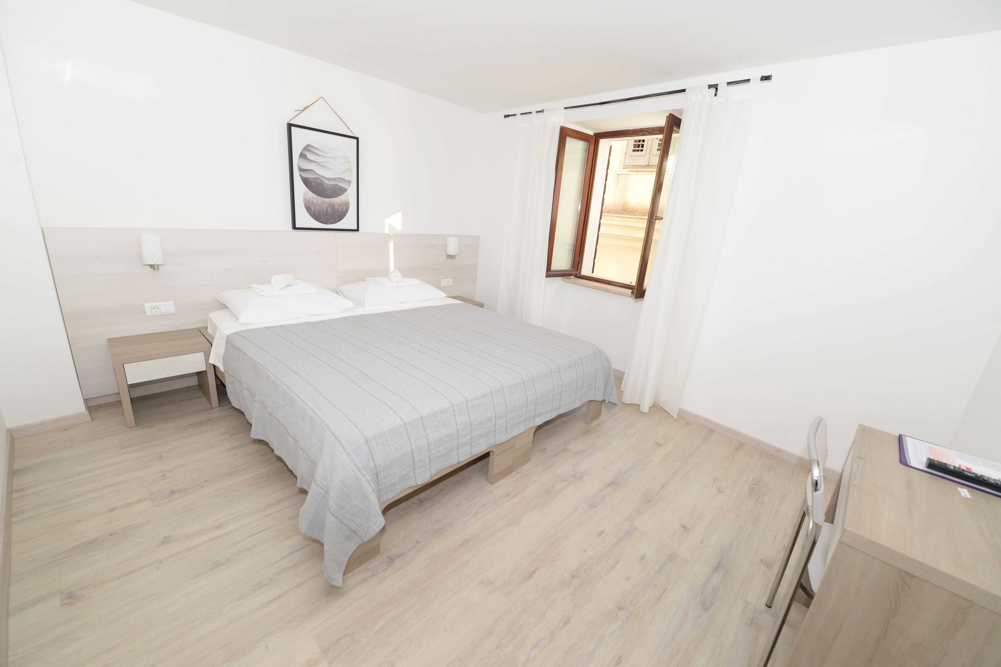 A modern bedroom with a bed, bedside tables, a nightstand, a window with curtains, and a framed picture on the wall.