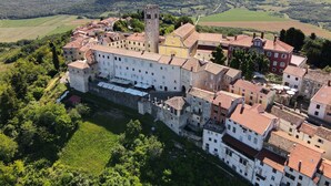 Vista aérea de un pueblo histórico con una torre destacada, rodeado de campos verdes exuberantes y colinas ondulantes.