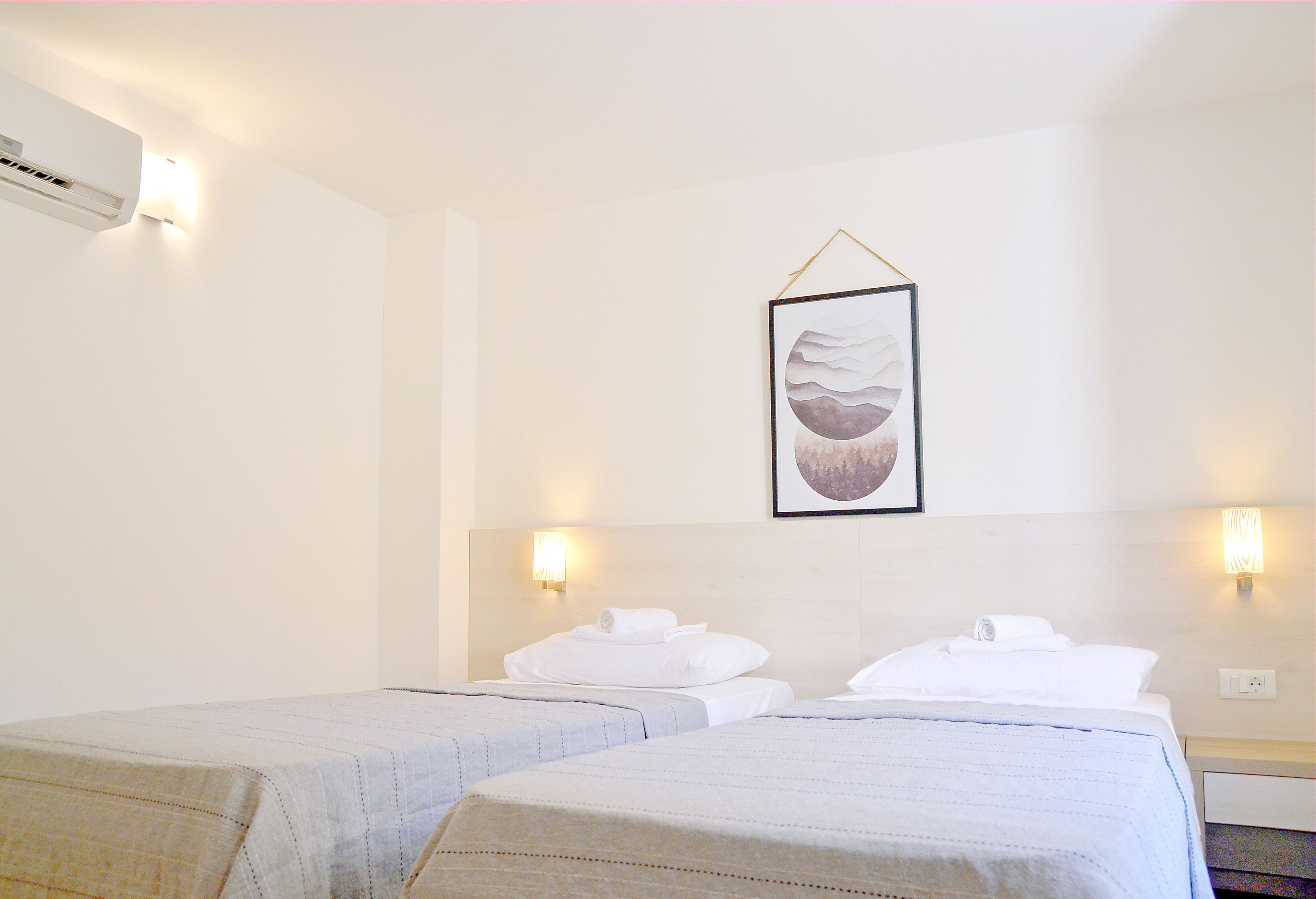 Een hotelkamer met twee bedden, een ingelijste afbeelding aan de muur en wandlampen.