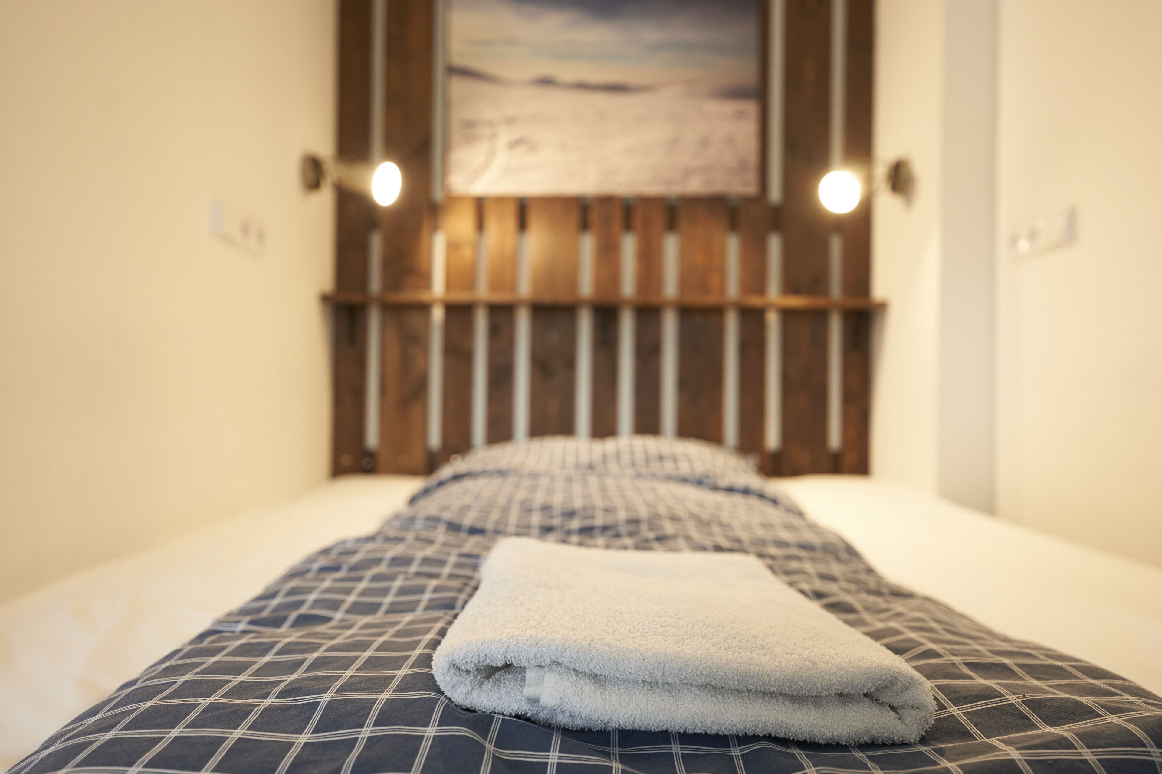 Een net opgemaakt bed met een geruit sprei en een opgevouwen witte handdoek.