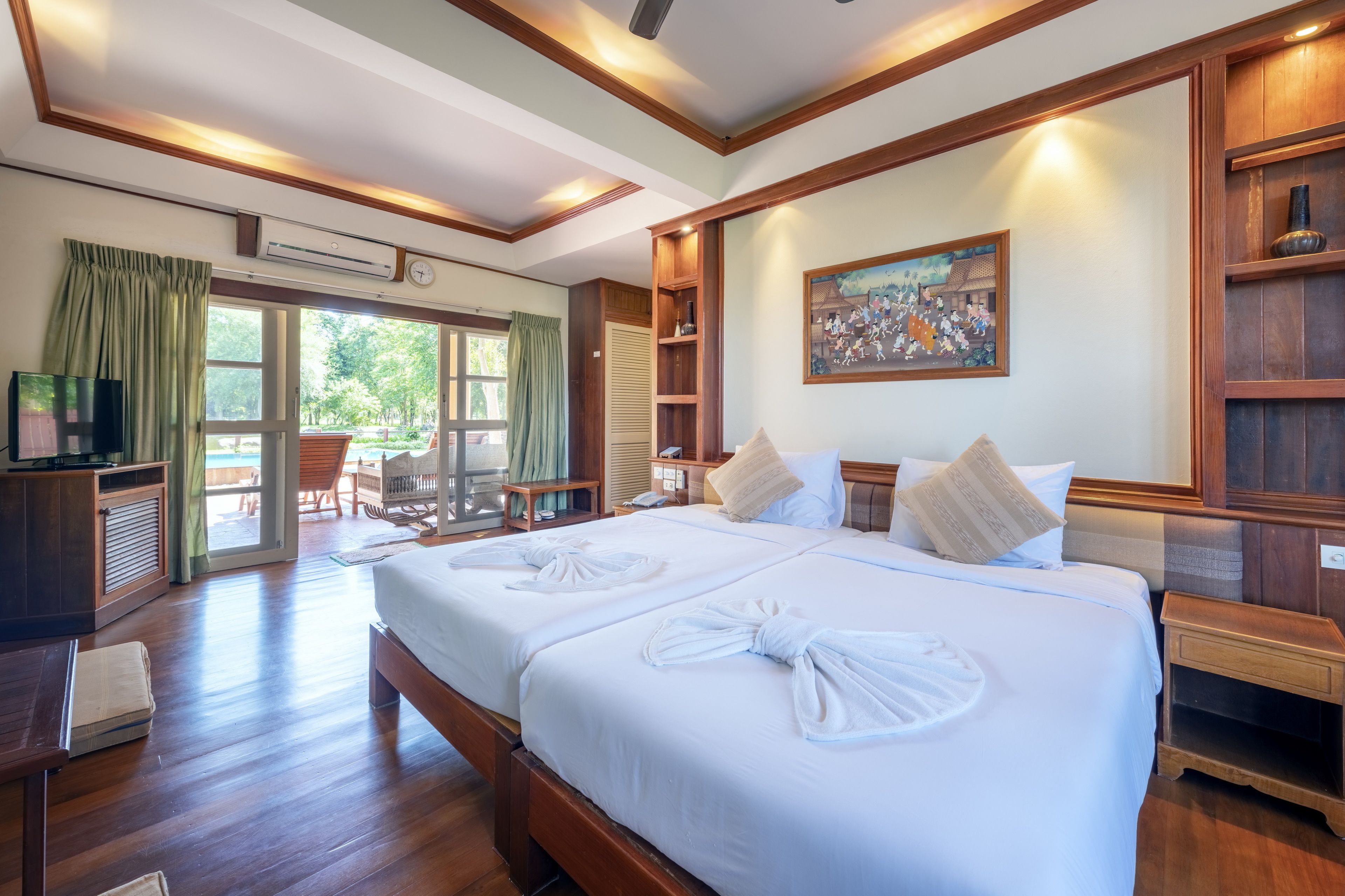 Habitación de hotel con dos camas, televisión, escritorio y balcón con vistas al exterior.
