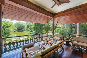 Un espacio de estar al aire libre con techo, muebles de madera y vista a un estanque y árboles.