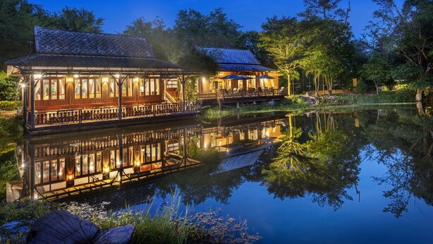 A traditional wooden building with a reflection in the water, surrounded by trees and a calm lake. - Vana Varin Resort Hua Hin (Hua Hin)