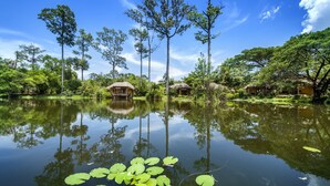 A serene lakeside setting with thatched-roof huts and tall trees reflecting in calm water. - Vana Varin Resort Hua Hin (Hua Hin)