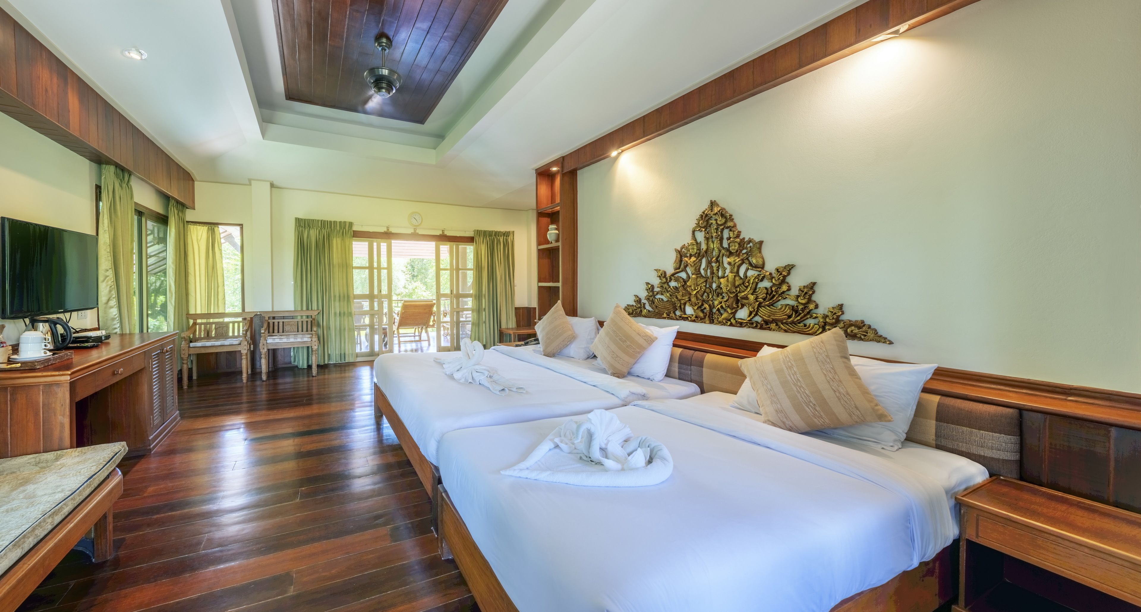 Une chambre d’hôtel avec deux lits, un plancher en bois, une tête de lit en bois, une télévision, un bureau et une chaise.