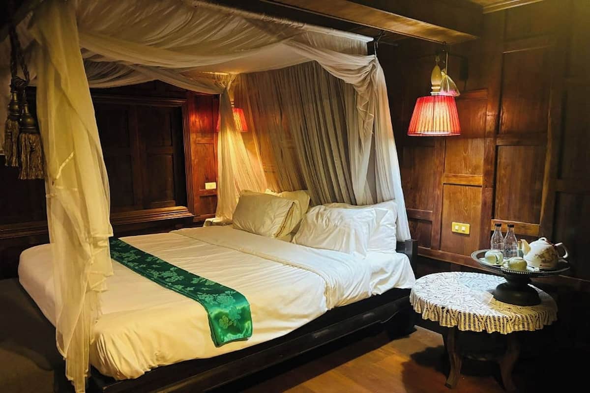 A four-poster bed with a canopy, a round table with a lace tablecloth, and a red lamp.