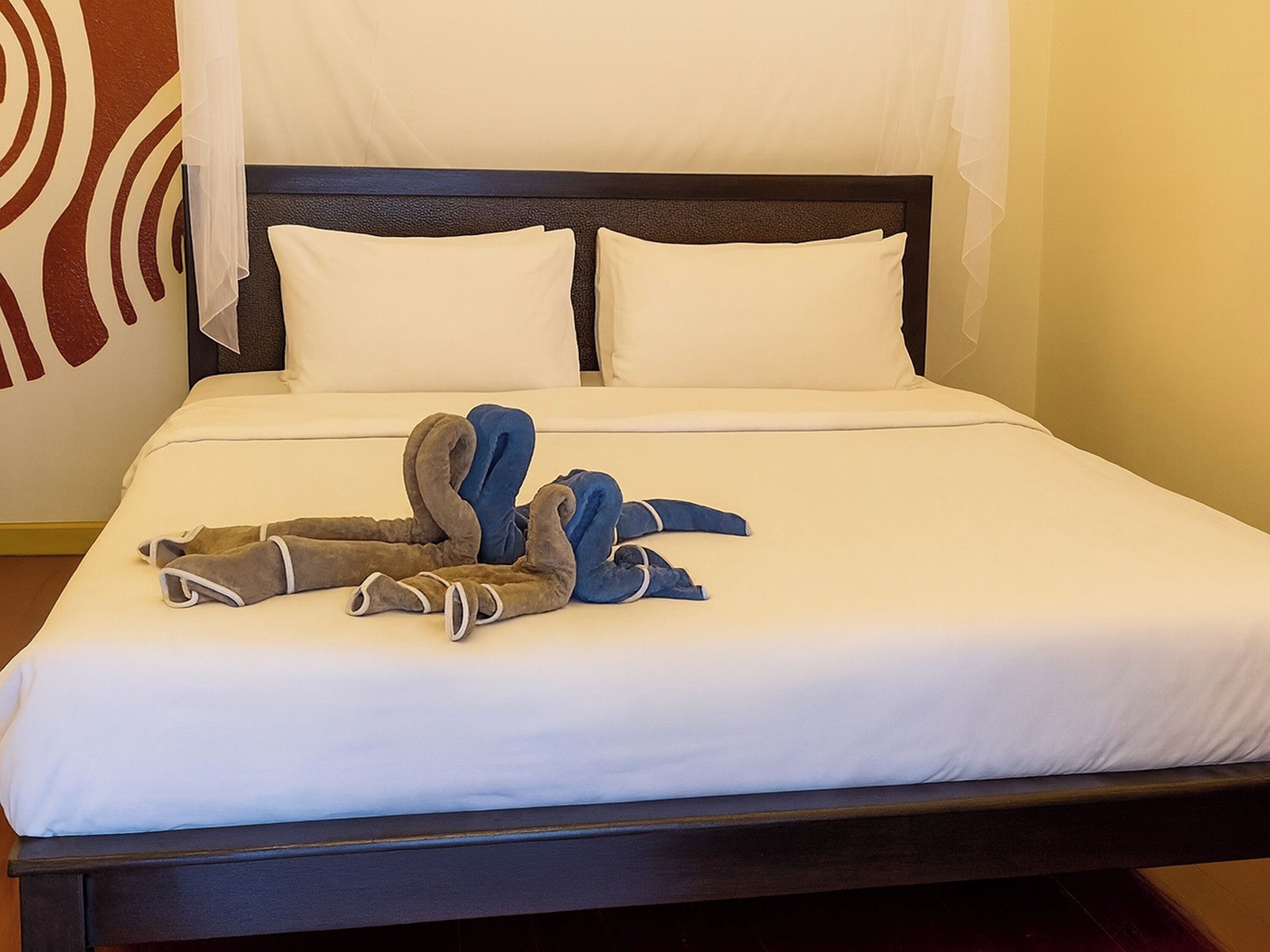 A neatly made bed with white linens and two pillows, a dark headboard, and a pair of folded towels on the bed.