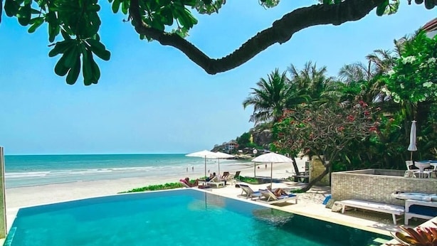 Ein klares, blaues Schwimmbecken mit Liegestühlen und Sonnenschirmen mit Blick auf einen Strand und den Ozean.