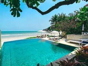 Une piscine d’un bleu éclatant, dotée de chaises longues et de parasols, qui offre une vue sur une plage et l’océan.