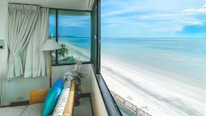 Ein Zimmer mit Blick auf einen Strand, ein Fenster mit Vorhängen, eine Lampe und ein Sofa.