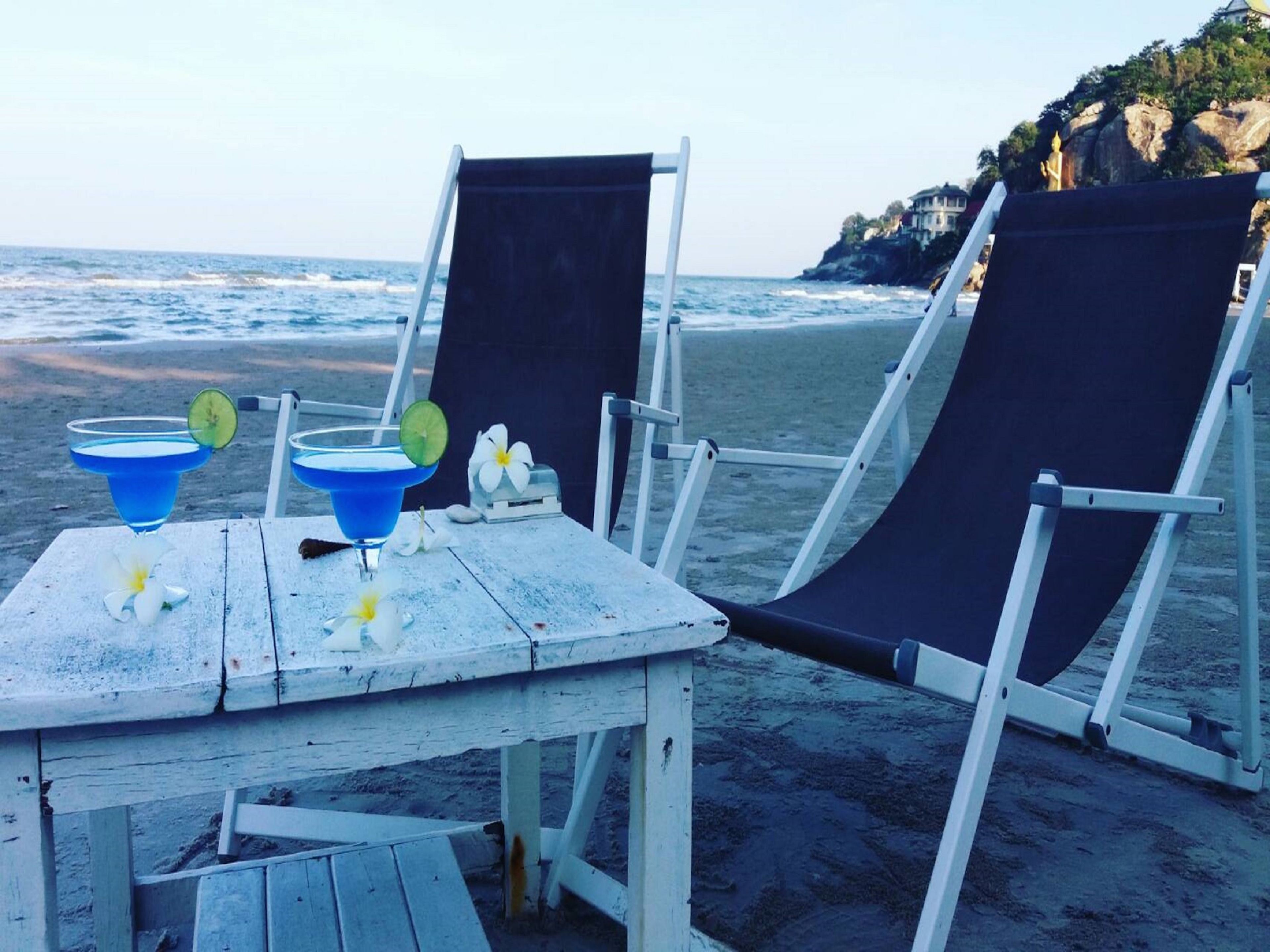 A beach setting with two lounge chairs and a table with drinks and flowers.