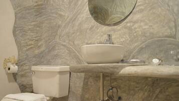 A bathroom with a marble wall, a sink, a toilet, and a mirror.