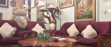 A living room with a large sofa, a wooden coffee table, and various decorative items including a large teddy bear and framed artwork on the walls.
