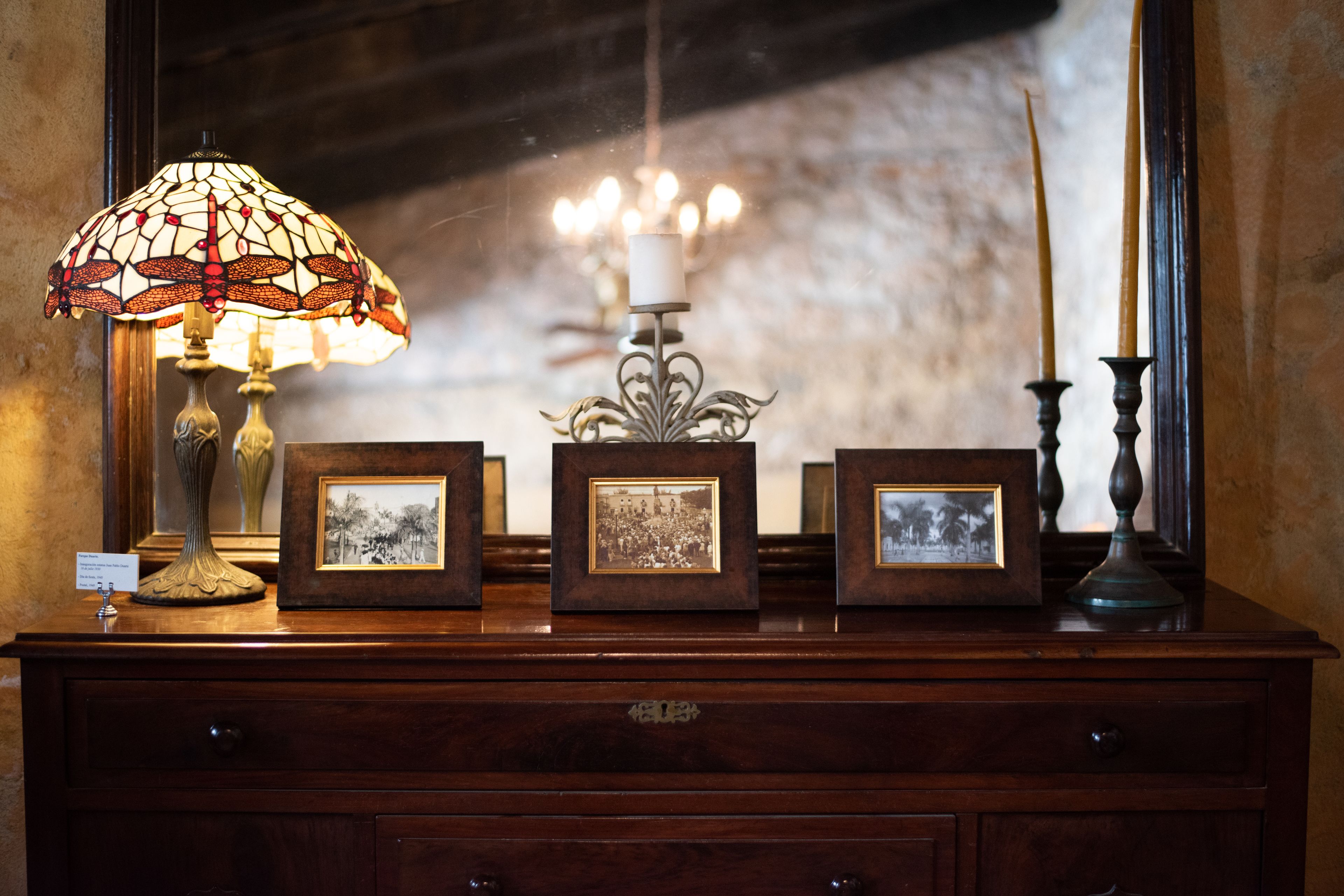 A wooden dresser with a stained glass lamp, framed photographs, and a candle holder.