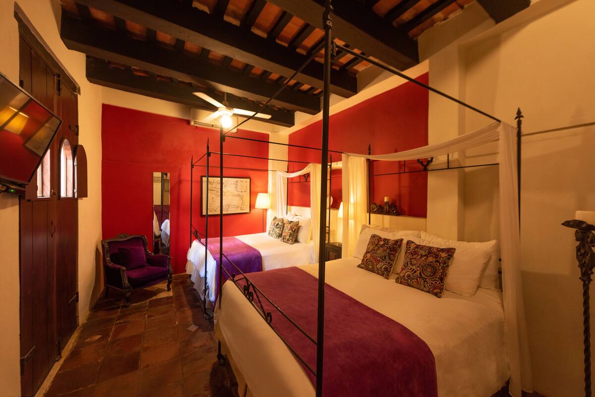 A four-poster bed with a canopy, two single beds, a chair, and a red wall.