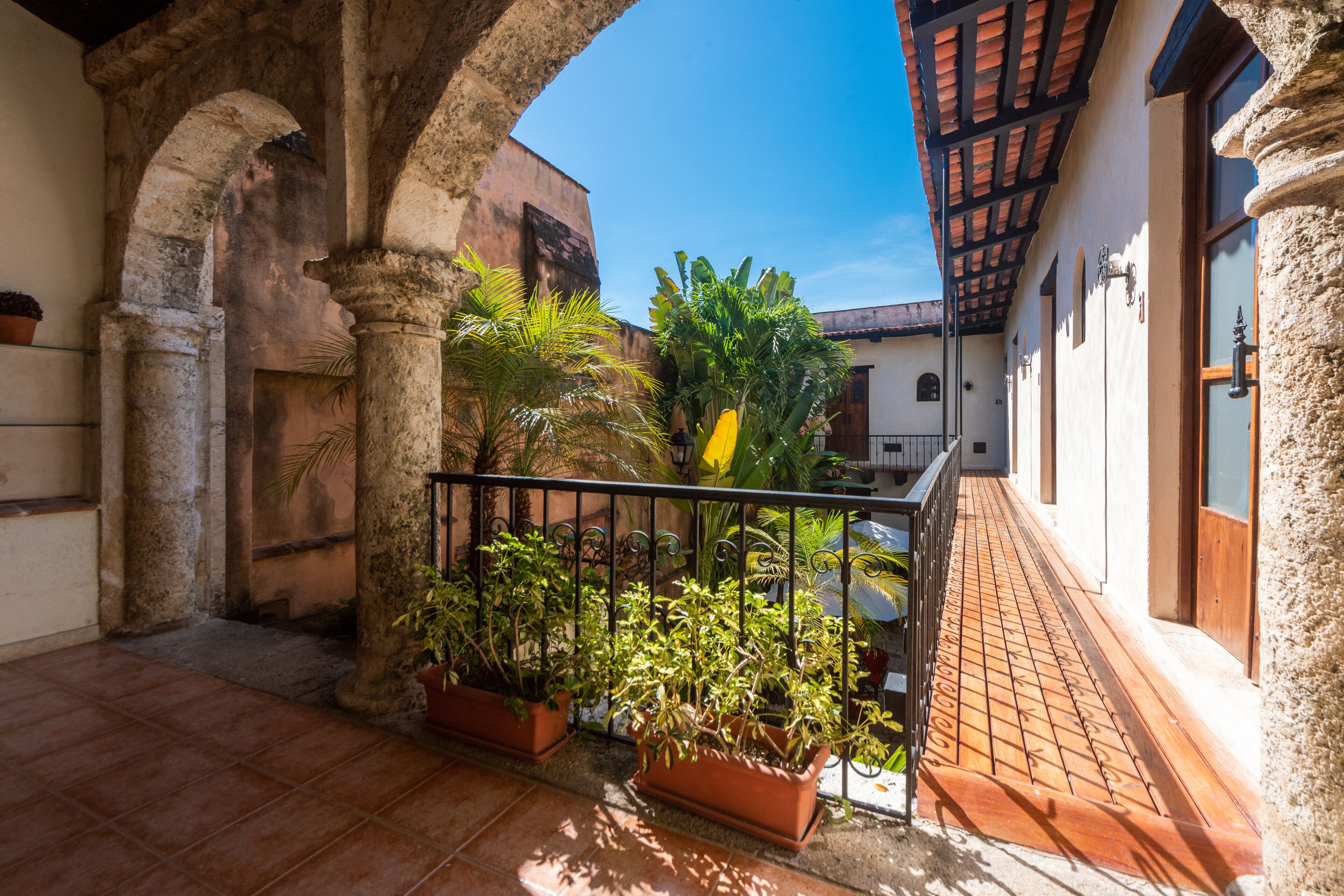 A courtyard with terracotta tiles, potted plants, and a wooden balcony.