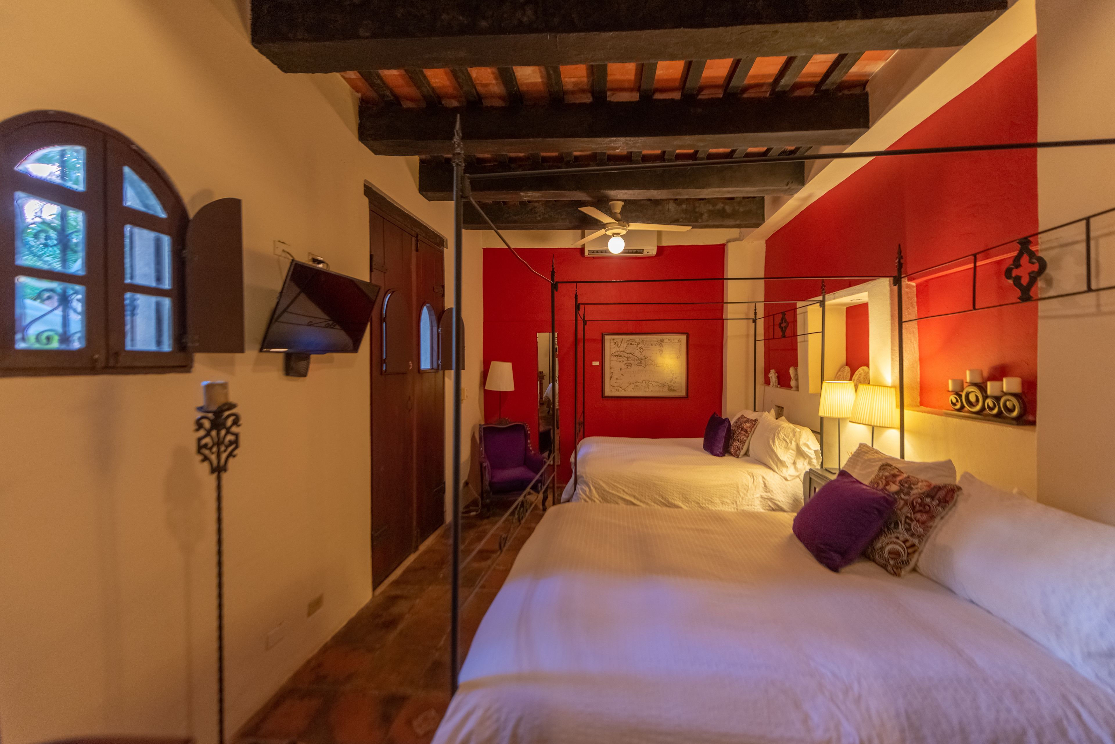 A hotel room with two beds, a red accent wall, a ceiling fan, and a window with a view.