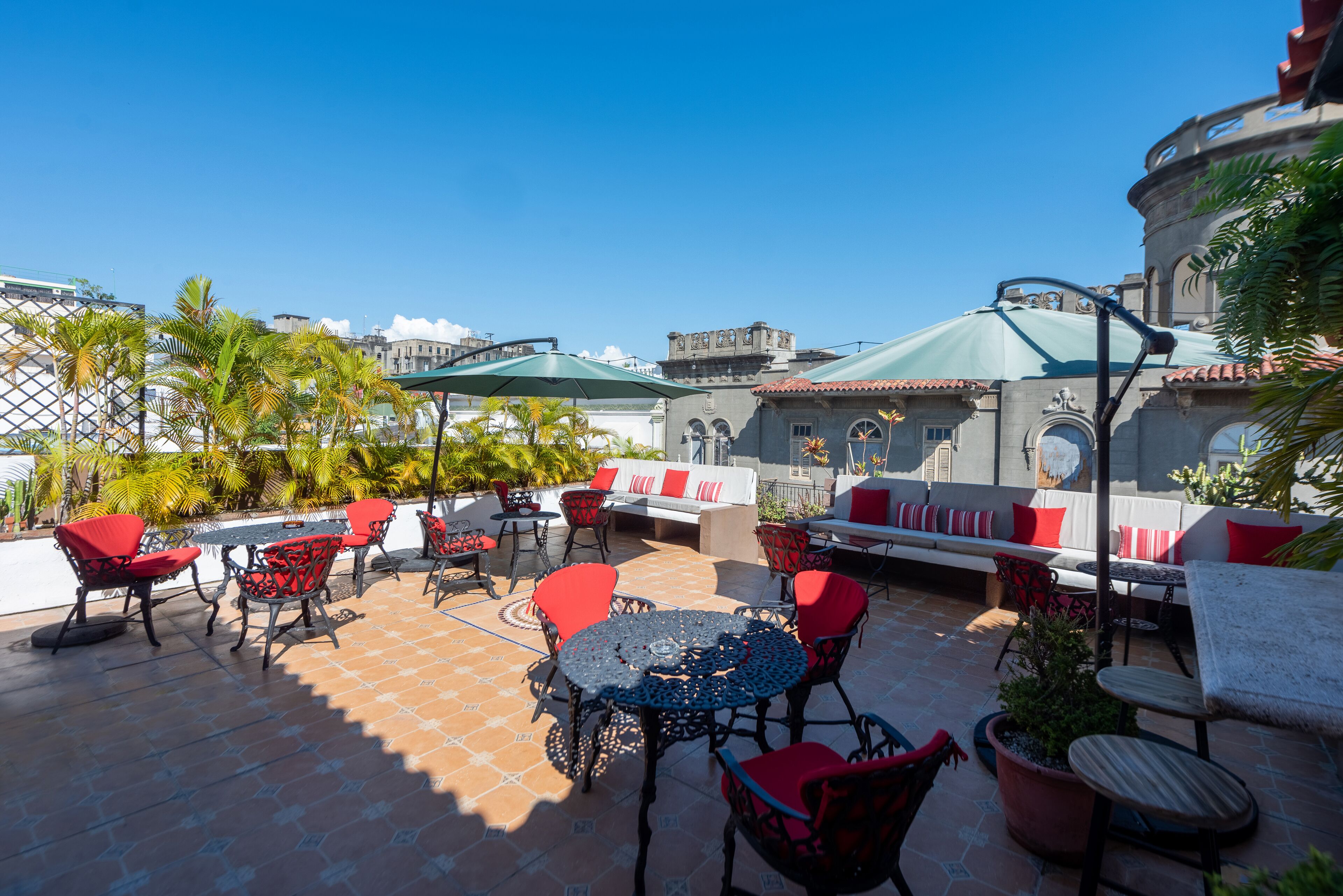An outdoor patio with red and black chairs, a round table, and a green umbrella.