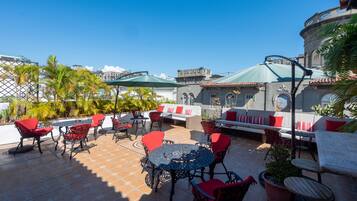 An outdoor patio with red and black chairs, a round table, and a green umbrella.