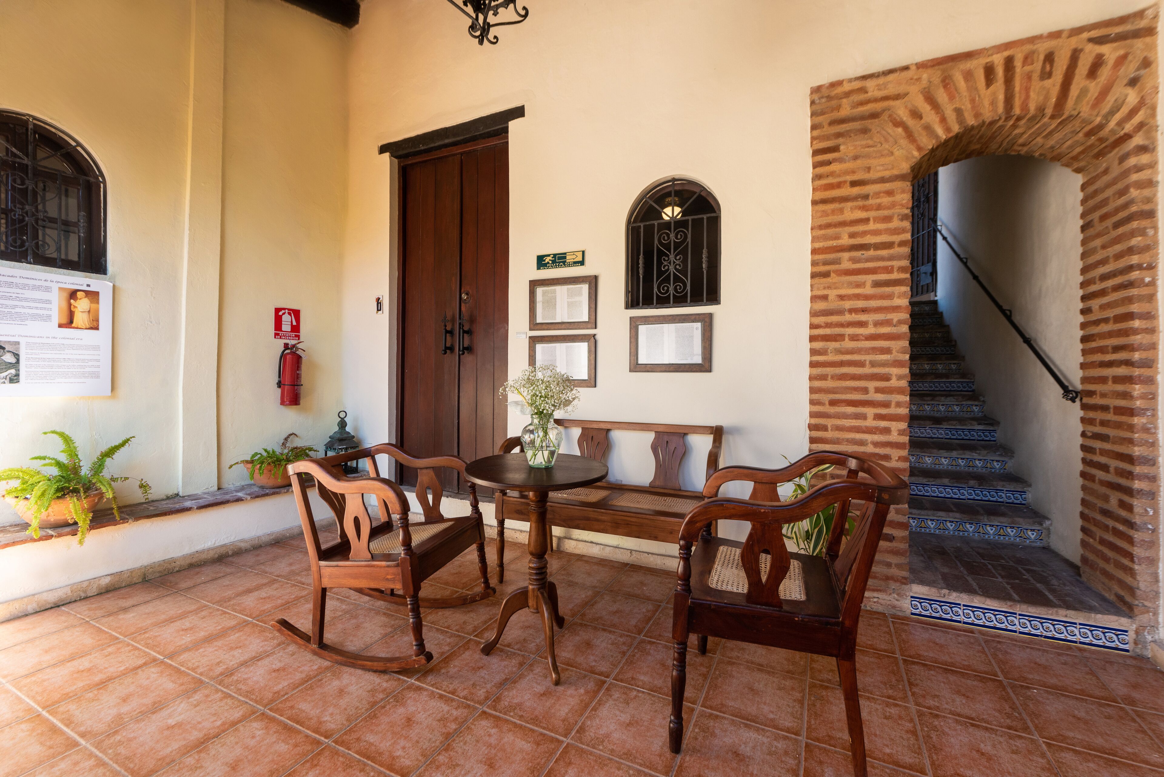 Un patio con mesa y sillas de madera, un banco, plantas en macetas y un extintor.