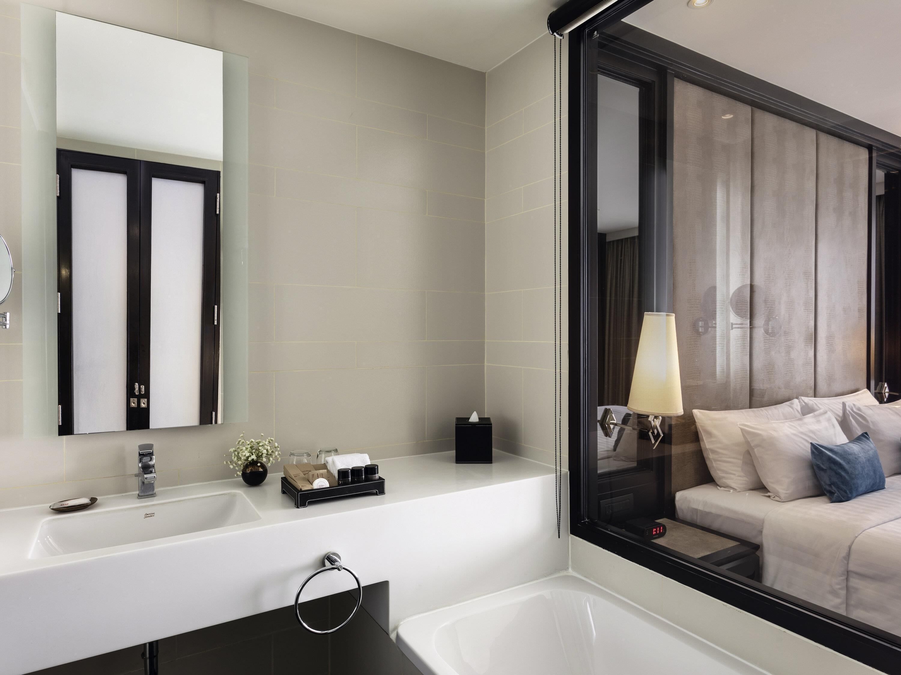 A modern bathroom with a large mirror, a bathtub, and a vanity with toiletries.