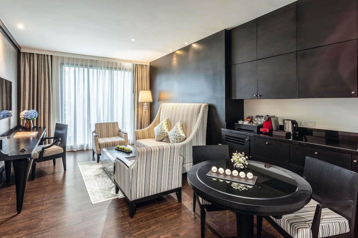 Una habitación de hotel moderna con zona de comedor, sofá, mesa de centro y kitchenette.