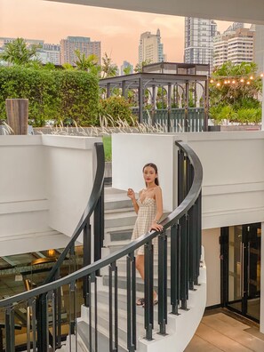 A woman on a curved staircase with a cityscape view in the background. - Mövenpick Hotel Sukhumvit 15 Bangkok (Bangkok)