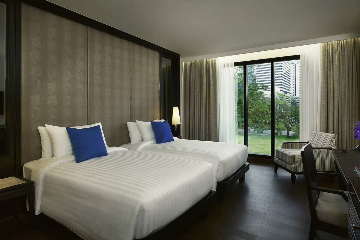 A hotel room with two beds, a desk, and a view of the outdoors.