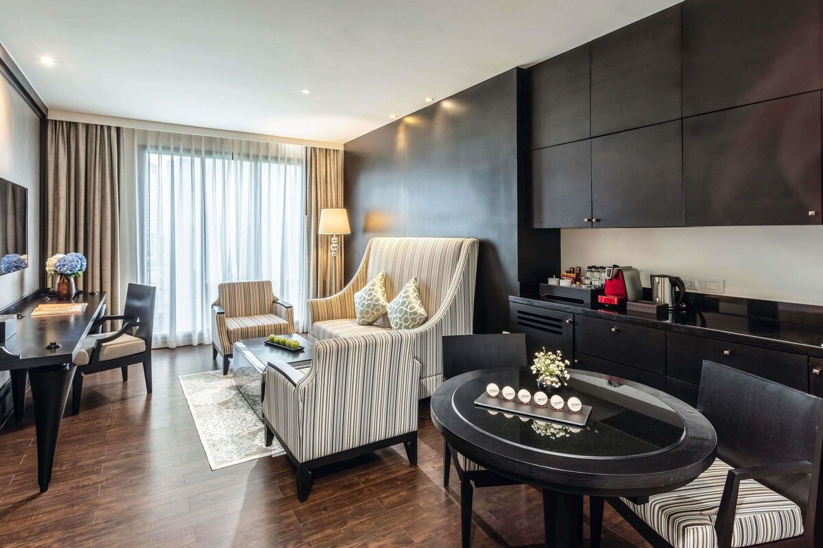 A modern hotel room with a dining area, a sofa, a coffee table, and a kitchen area.