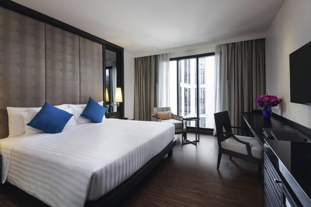 A hotel room with a large bed, a desk, a chair, a TV, and a window with curtains.