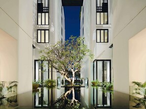A modern building with a central tree, large windows, and indoor plants. - Mövenpick Hotel Sukhumvit 15 Bangkok (Bangkok)