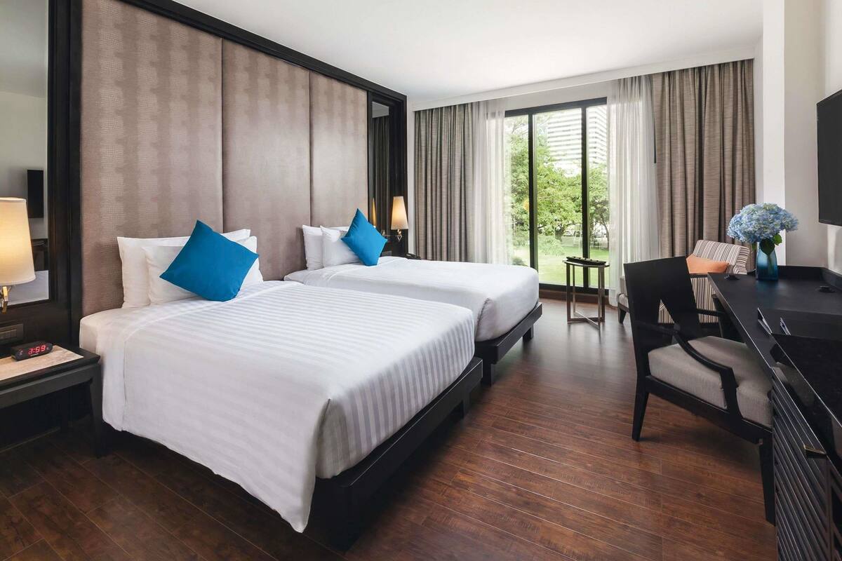 A hotel room with two beds, a desk, a chair, a TV, and a window with curtains.