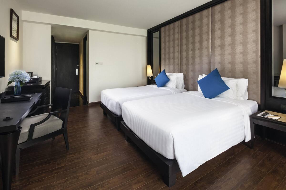 A hotel room with two beds, a desk, a chair, and a large mirror.