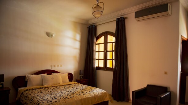 Een slaapkamer met een bed, een stoel, een raam met gordijnen en een airconditioning.