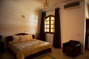 A bedroom with a bed, a chair, a window with curtains, and an air conditioning unit. - Residence Vanestelle (Abidjan)