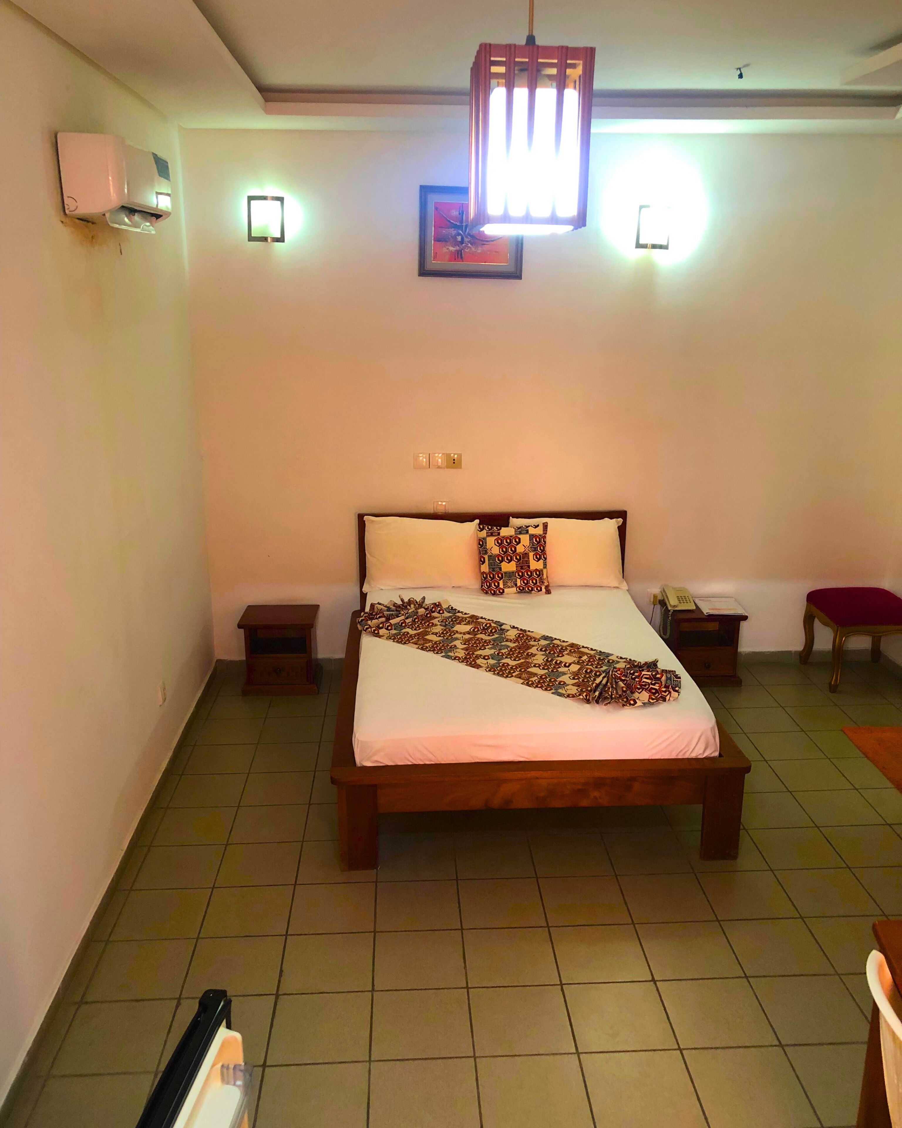 Een slaapkamer met een groot bed, twee nachtkastjes, een bijzettafeltje, een rode stoel en een plafondventilator.
