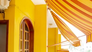 Een kamer in felle kleuren, met gele wanden, een groot raam met een gebogen bovenkant en een gestreept luifel.