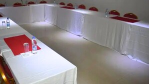 Een vergaderruimte met een lange tafel, rode stoelen en waterflesjes.