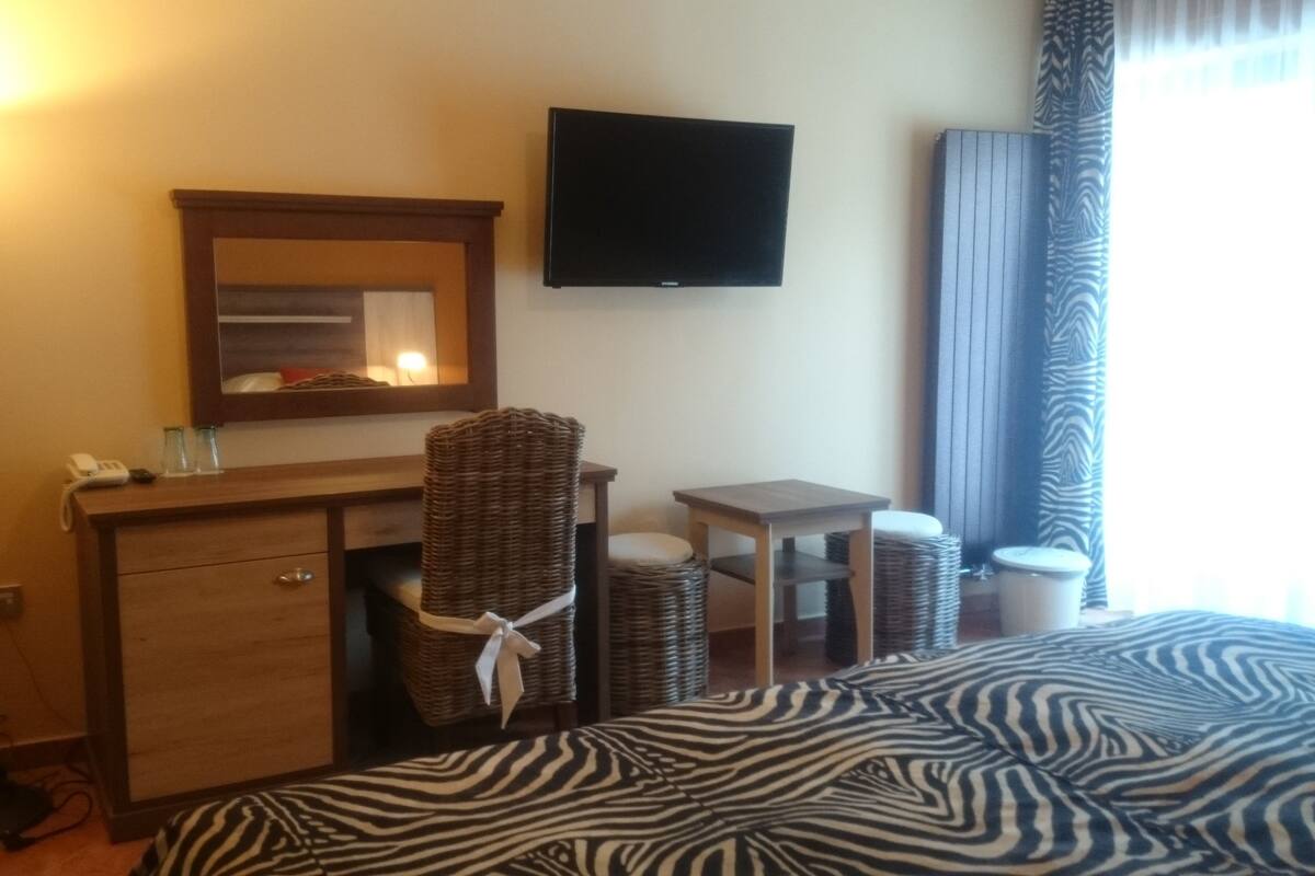 A hotel room with a bed, a desk, a chair, a mirror, a television, and a lamp.