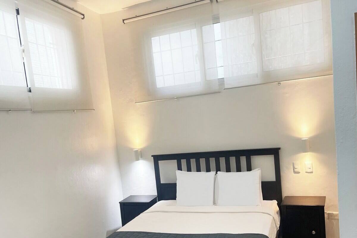 Ein modernes Schlafzimmer mit einem dunklen Holzbett, weißer Bettwäsche und zwei Nachttischen mit Wandleuchten.