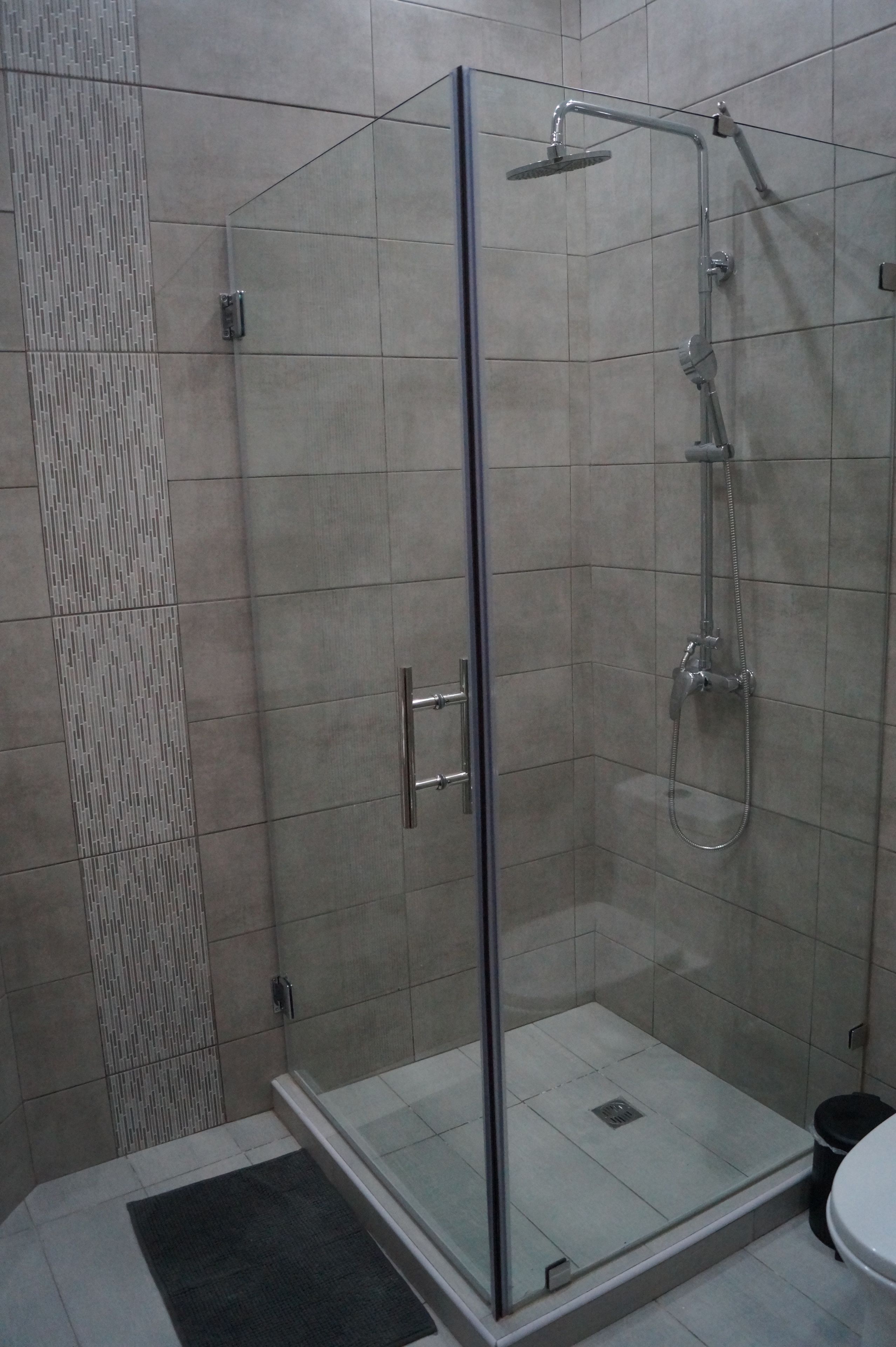 A glass-enclosed shower stall with a handheld showerhead and a wall-mounted faucet.