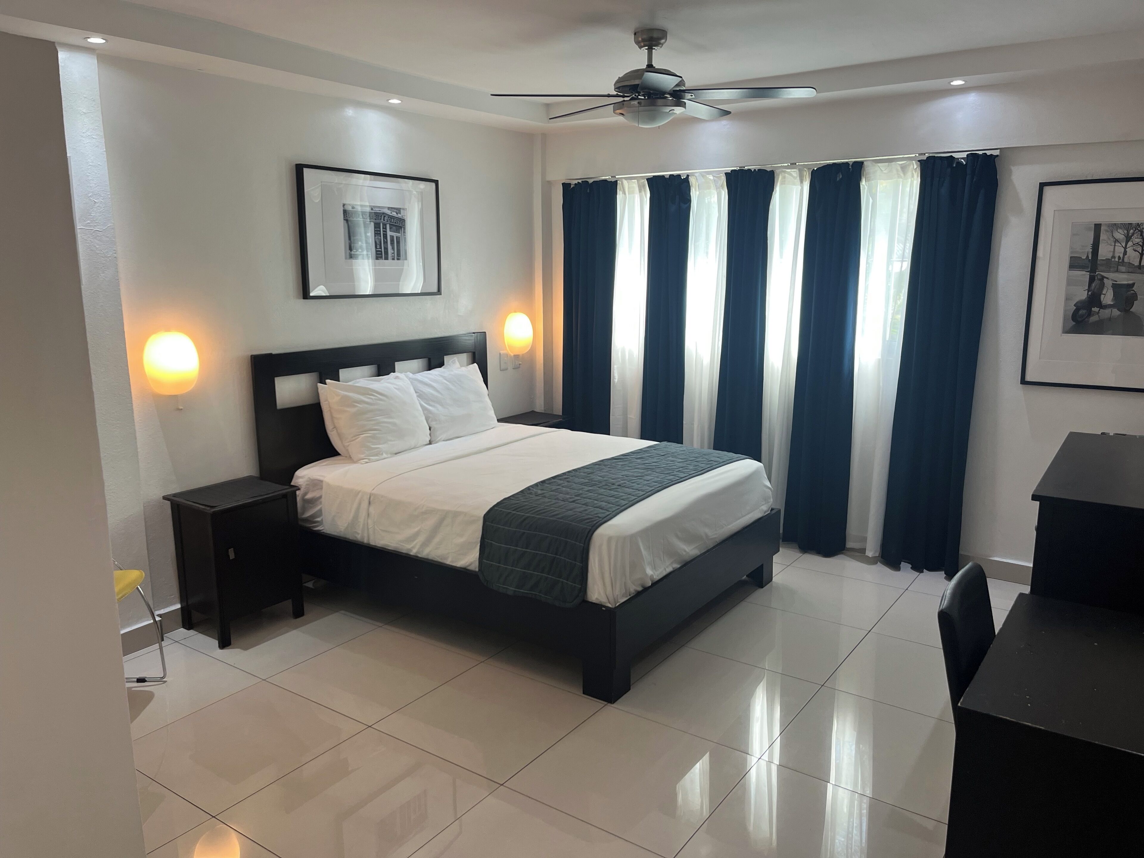 A neatly arranged bedroom with a bed, a ceiling fan, and a nightstand with a lamp.