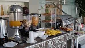 Un buffet proposant une variété de plats et de boissons, notamment une machine à café, des bols de céréales et un présentoir de fruits.