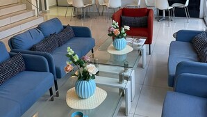 Un salon moderne avec des canapés bleus, une table basse en verre et un fauteuil rouge. Des tableaux encadrés ornent le mur, et un escalier mène à un autre niveau.