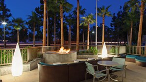 An outdoor seating area with a fire feature, surrounded by palm trees and a railing. - SpringHill Suites Anaheim Maingate (Anaheim)